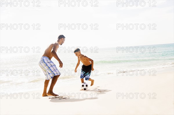 Father and son (10-11) playing soccer on beach