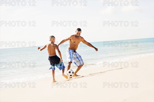 Father and son (10-11) playing soccer on beach