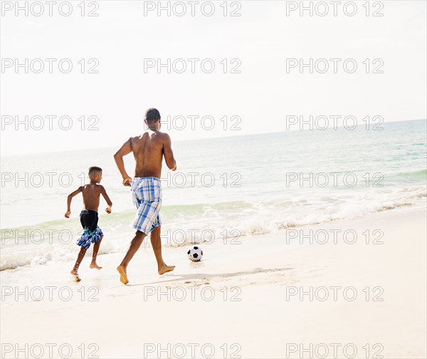 Father and son (10-11) playing soccer on beach