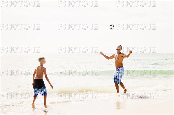 Father and son (10-11) playing soccer on beach