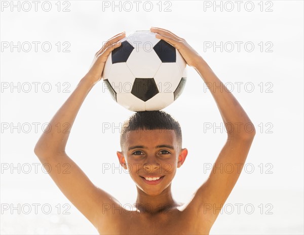 Boy (10-11) holding soccer ball on head