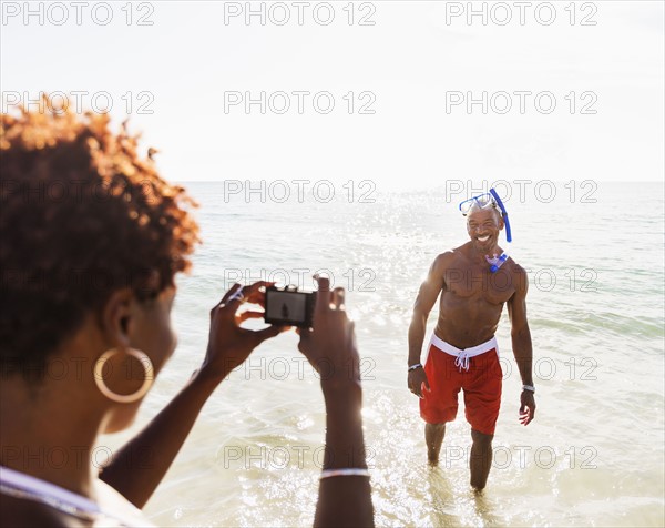 Woman photographing man on beach