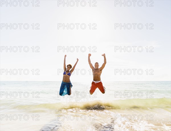 Mature couple jumping in sea with arms raised