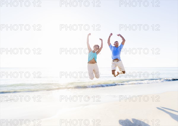 Mature couple jumping in sea with arms raised