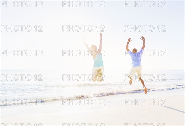 Mature couple jumping in sea with arms raised