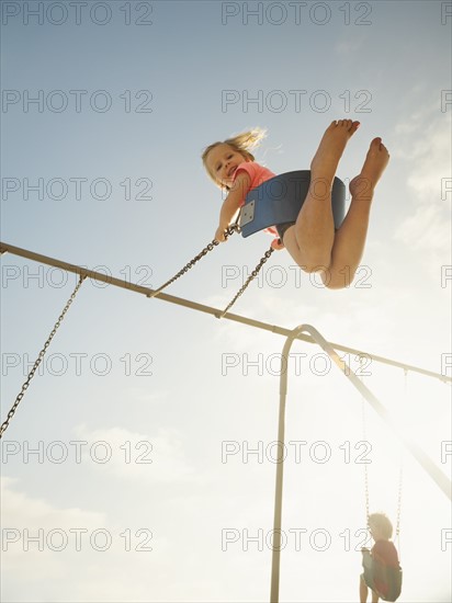 Girl (4-5) and boy (2-3) swinging on beach