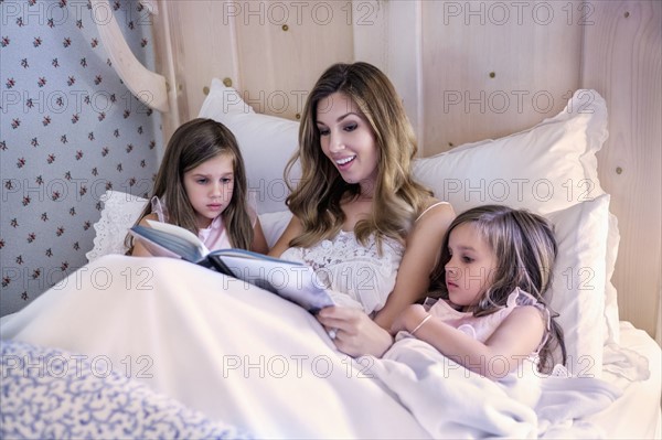 Mother reading bedtime story to her twin daughters (4-5)