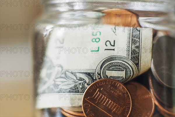 Studio shot of jar filled with coins and one dollar banknote, close up