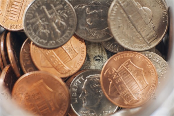 Studio shot of jar filled with coins and one dollar banknote, close up