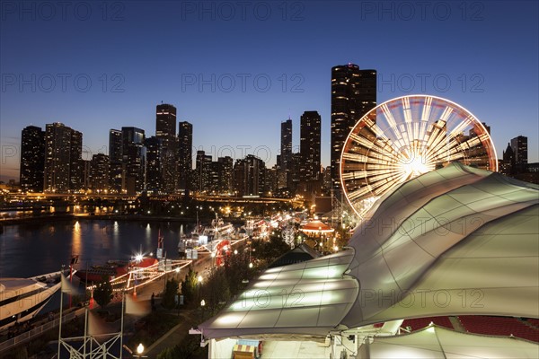 Illuminated ferris wheel with skyscrapers in background