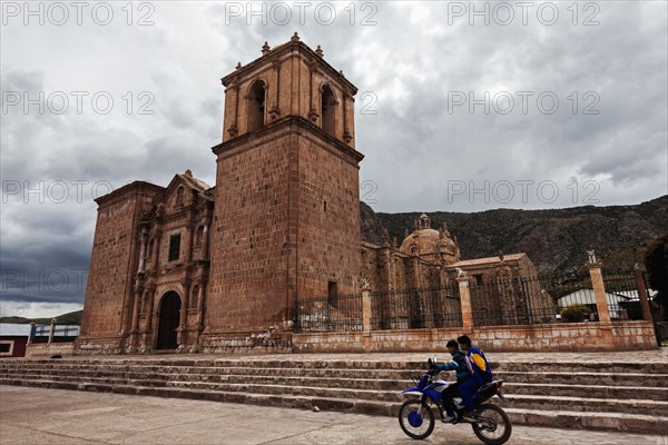 Two boys on motorcycle passing near old church