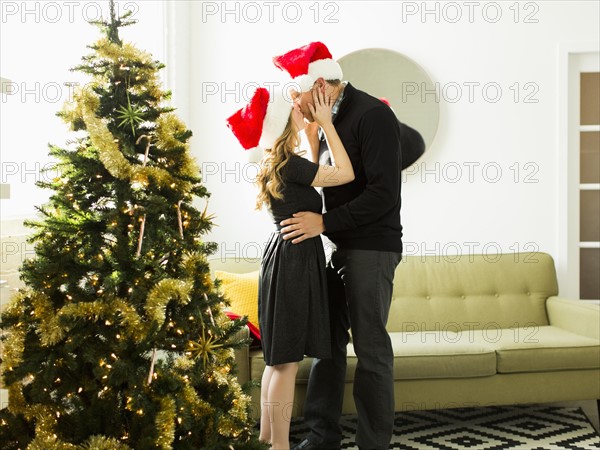 Young woman and man wearing Santa hats kissing