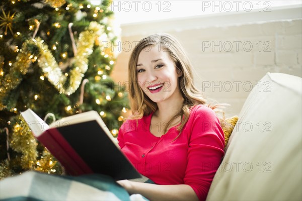 Young woman reading book on sofa at Christmas time
