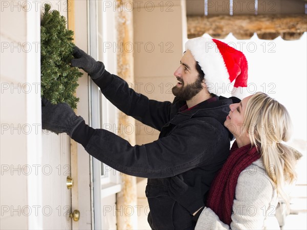 Young couple hanging wreath on door