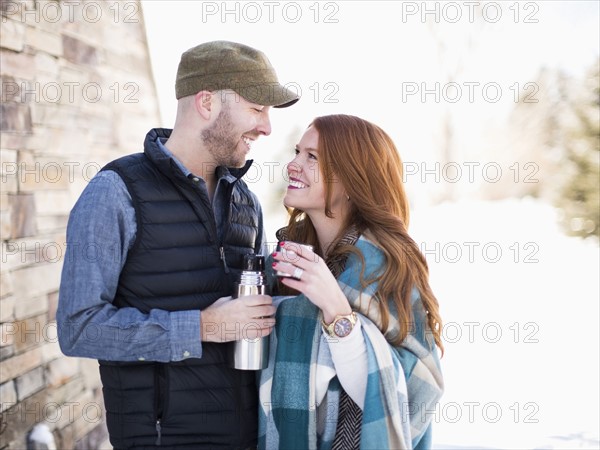 Mid adult couple looking face to face and having drink from vacuum flask