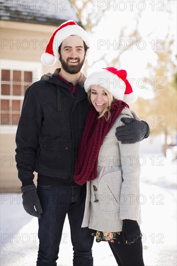 Portrait of young couple in santa hats in front of house