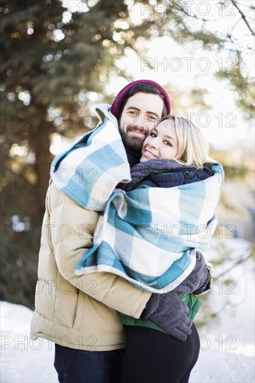 Couple wrapped in blanket hugging outdoors