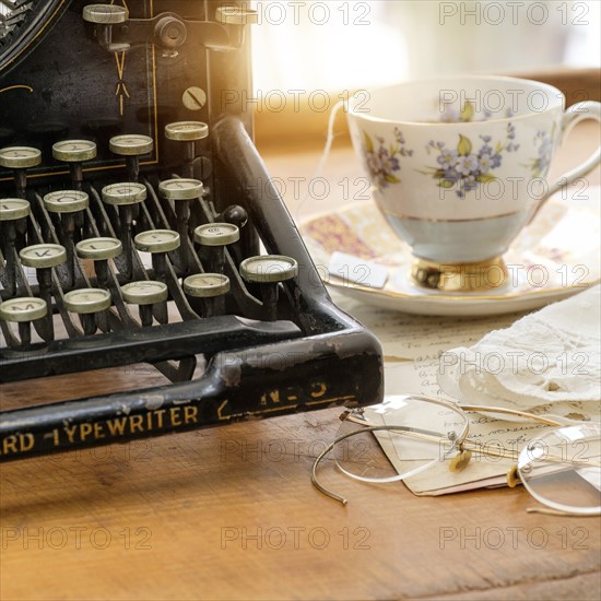 Studio shot of antique typewriter with teacup and eyeglasses.