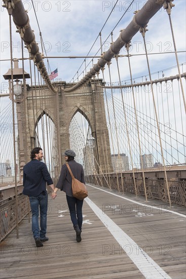 Couple holding hands and walking on Brooklyn Bridge. Brooklyn, New York.