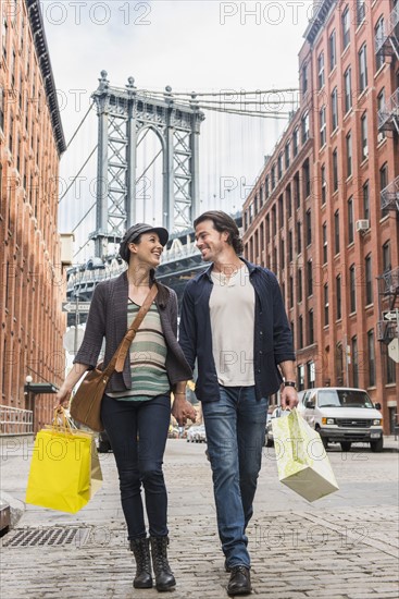 Couple walking on street, Brooklyn Bridge in background. Brooklyn, New York.