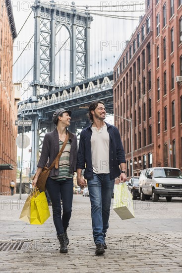 Couple walking on street, Brooklyn Bridge in background. Brooklyn, New York.