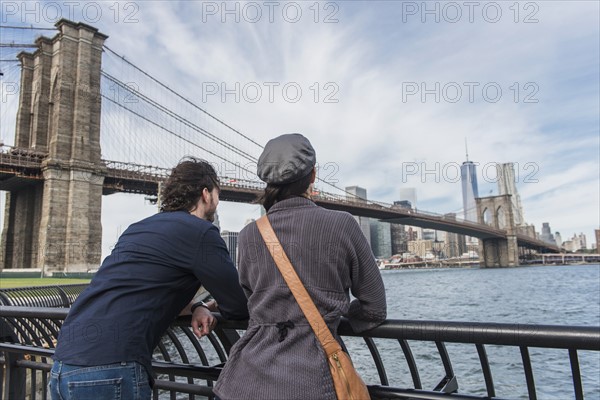 Couple leaning against railing and looking at Freedom Tower. Brooklyn, New York.