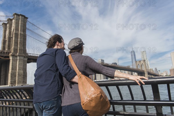 Couple leaning against railing and looking at Freedom Tower. Brooklyn, New York.