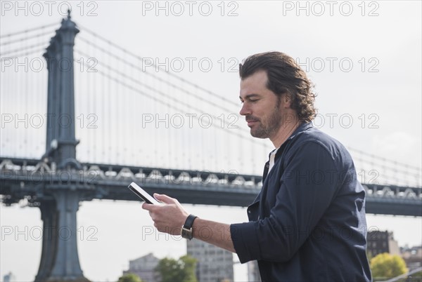 Man using tablet pc, Manhattan Bridge in background. Brooklyn, New York.