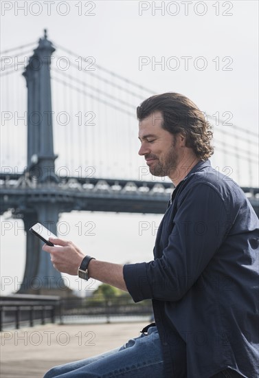 Man using tablet pc, Manhattan Bridge in background. Brooklyn, New York.