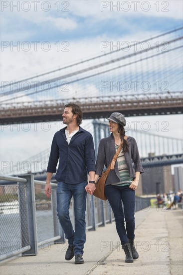 Couple walking on promenade, Brooklyn Bridge in background. Brooklyn, New York.