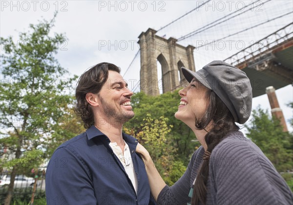 Happy couple standing against Brooklyn Bridge. Brooklyn, New York.