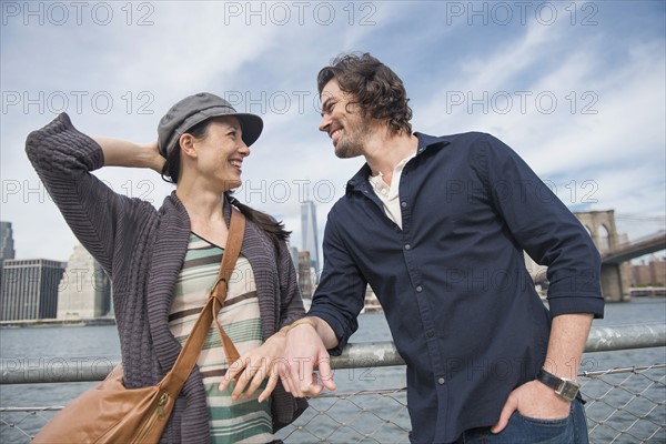 Happy couple standing and leaning against railing. Brooklyn, New York.