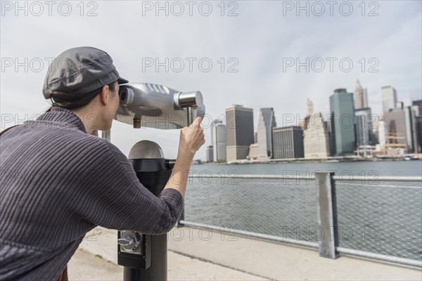 Woman watching cityscape through coin-operated binoculars. Brooklyn, New York.