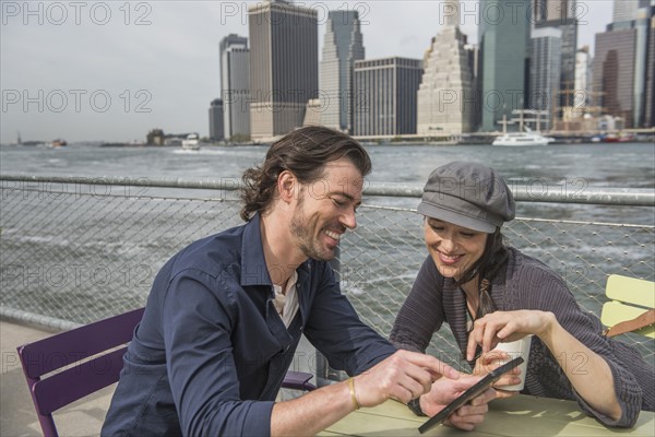 Happy couple sitting and using tablet pc with cityscape in background. Brooklyn, New York.