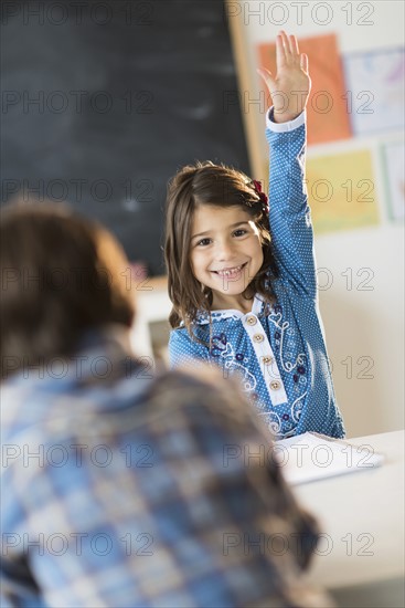 Pupils (6-7) learning in classroom, Girl (6-7) raising hand.