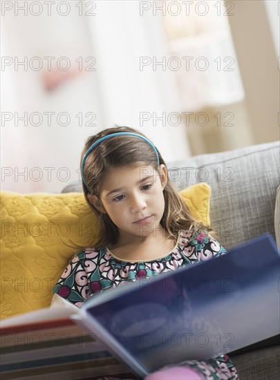 Girl (6-7) reading book at home.