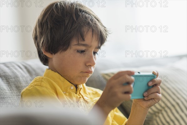 Boy (6-7) sitting on sofa and using cell phone.