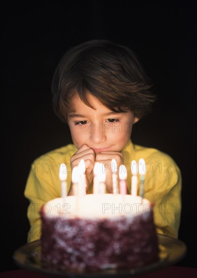Portrait of boy (6-7) thinking of birthday wishes, Looking at birthday cake.