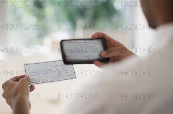 Man taking photo of banking check with cell phone.