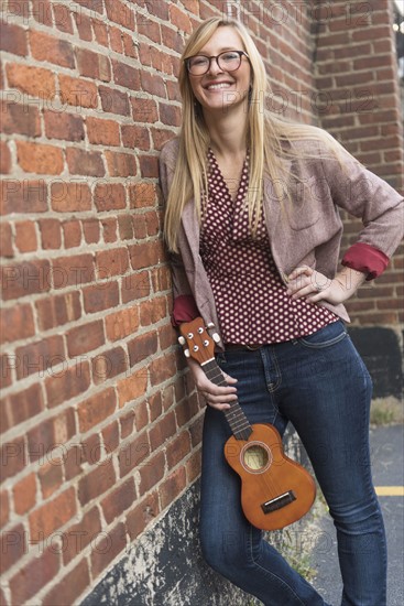 Woman standing against brick wall with ukulele.