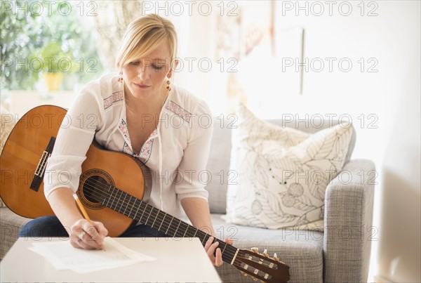 Woman sitting on sofa with acoustic guitar and writing.