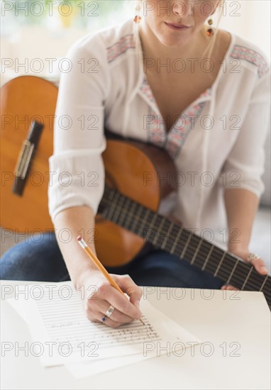 Woman sitting on sofa with acoustic guitar and writing.