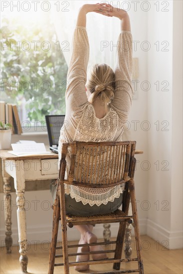 Rear view of woman stretching in front of laptop.