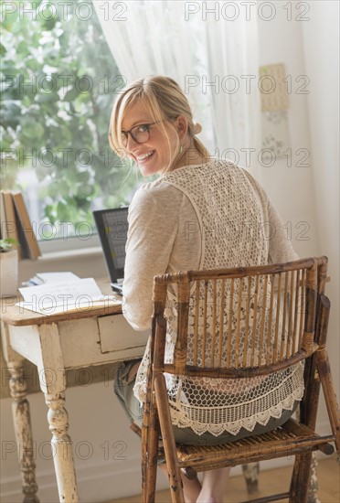Smiling woman sitting at desk and looking over shoulder.