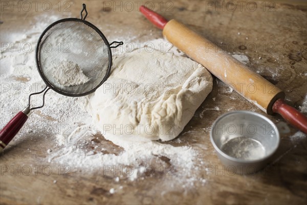 Rolling pin, Strainer and dough on kitchen counter.