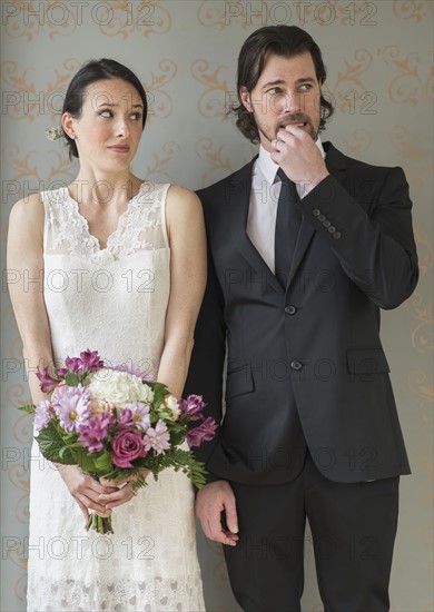 Anxious bride and groom posing with bunch of flowers.