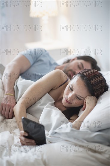 Couple in bed, woman reading on digital tablet and man sleeping.