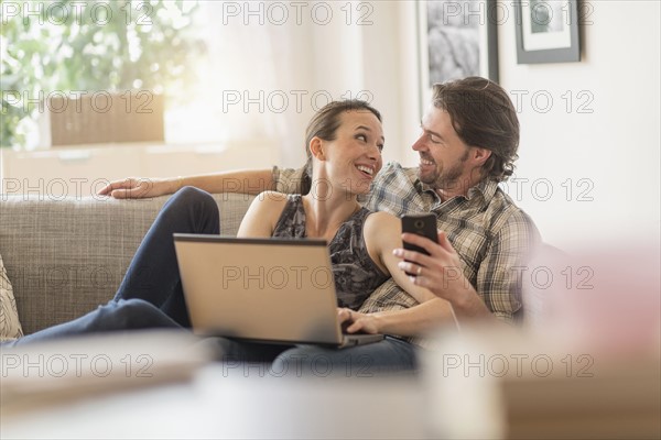 Cheerful couple on sofa with laptop and mobile phone.