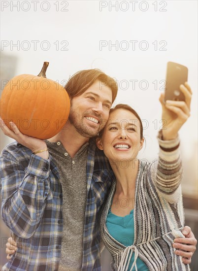 Couple taking selfie with mobile phone, man holding pumpkin.