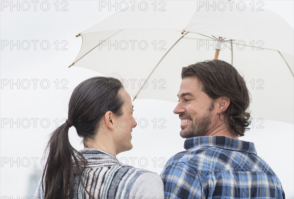 Rear view of couple under umbrella.